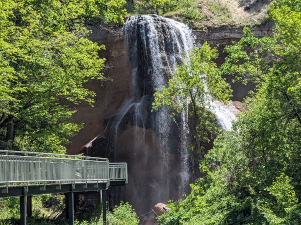 Smith Falls pours down a dark rock face into a leafy canyon beside a raised metal viewing walkway.