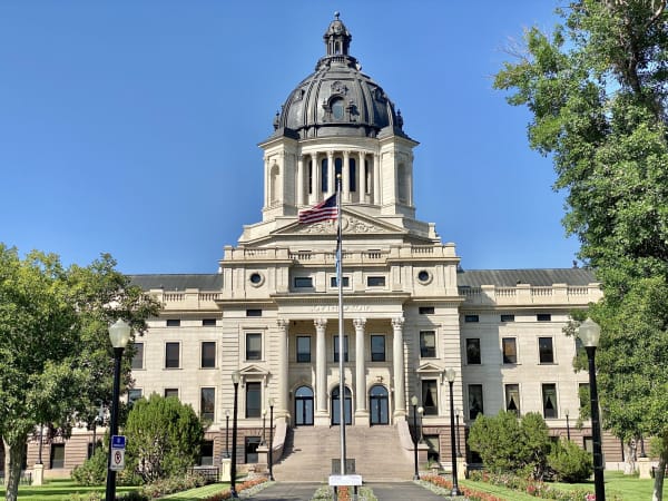 The domed South Dakota State Capitol in Pierre, seen up its front walk between trees and flower beds