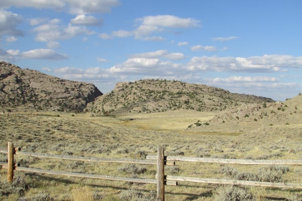 The notch of Devil's Gate cut through a granite ridge, seen across sagebrush range behind a rail fence