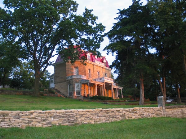 The limestone ranch house of the Spring Hill Ranch behind a dry-stone wall and shade trees.