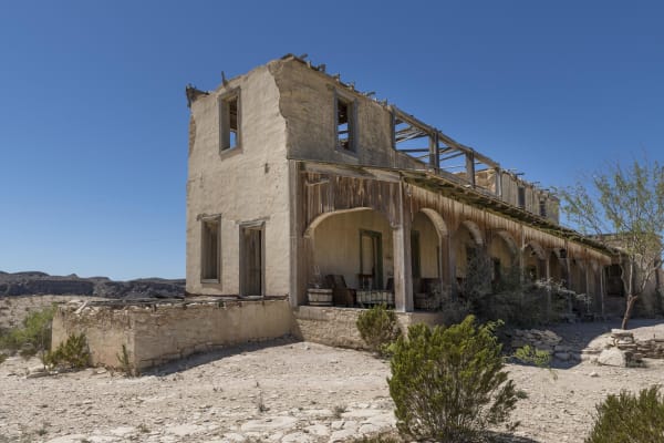 The roofless stone and adobe ruins of an old two-story building with a columned porch in the Terlingua ghost town.