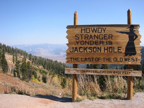 A carved wooden sign at the summit of Teton Pass reading Howdy Stranger, Yonder Is Jackson Hole, with the pass elevation of 8,431 feet beneath it and the valley spread out below