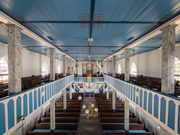The long nave of St. Paul Lutheran Church at Serbin, with blue and white galleries, white columns and dark wooden pews.