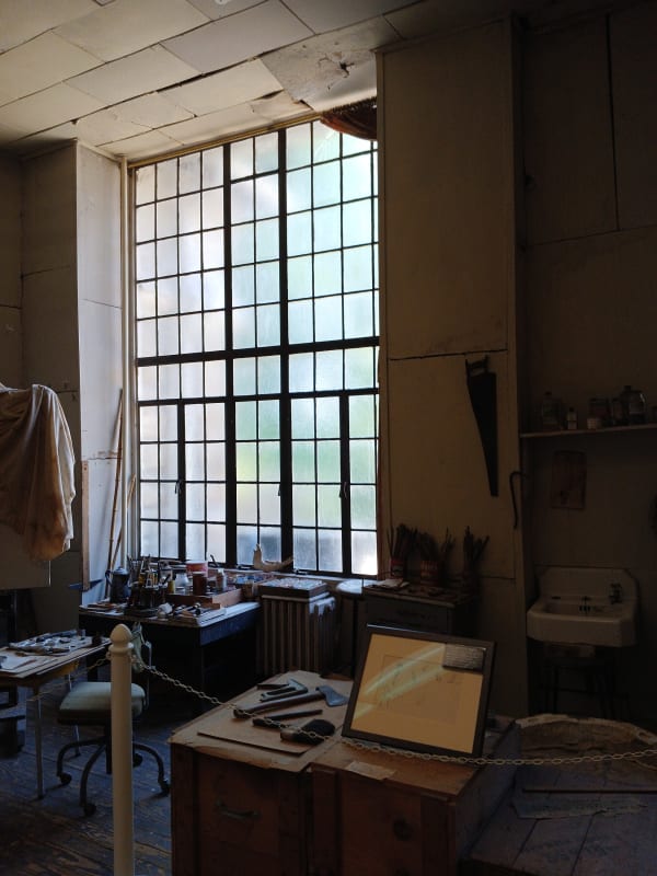 The tall multi-paned north window lighting the studio where Thomas Hart Benton worked, with his worktable and supplies below.