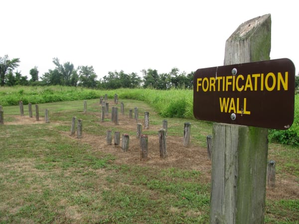 A wooden sign reading Fortification Wall beside rows of short posts that mark the line of the old palisade at Towosahgy State Historic Site.