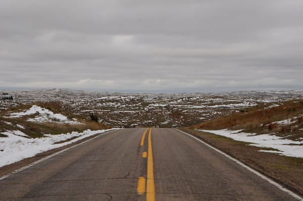 A two-lane road runs into Sandhills patched with melting snow at Valentine National Wildlife Refuge.