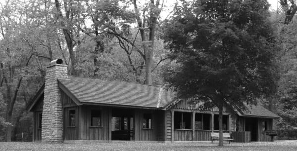 A black and white view of the stone and timber shelter building in the woods at Van Meter State Park.