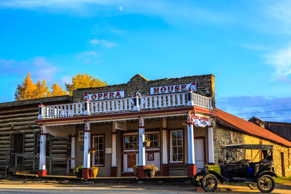 The Opera House in Virginia City, log and stone under a painted sign and porch, a Model T parked in front and autumn cottonwoods behind