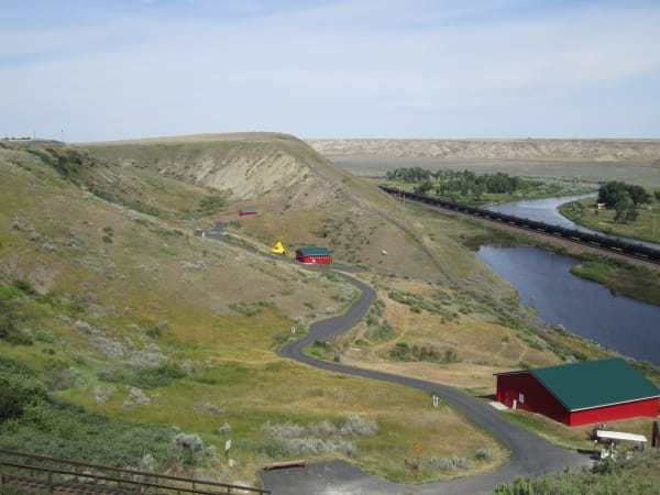 The Milk River breaks at Wahkpa Chu'gn, a road winding down a grassy coulee to red buildings beside the river