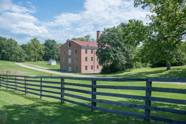 The three-story brick Watkins Woolen Mill seen across a pasture and a dark board fence.