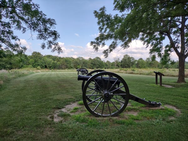 A Civil War cannon on the mown grass under oak trees at Wilsons Creek National Battlefield.