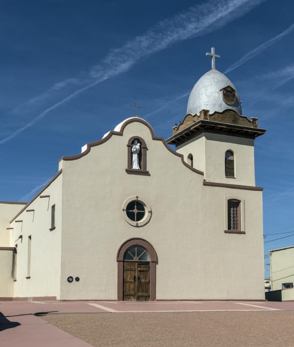 The cream-colored facade of the Ysleta Mission in El Paso, with its silver-domed bell tower and arched wooden door.