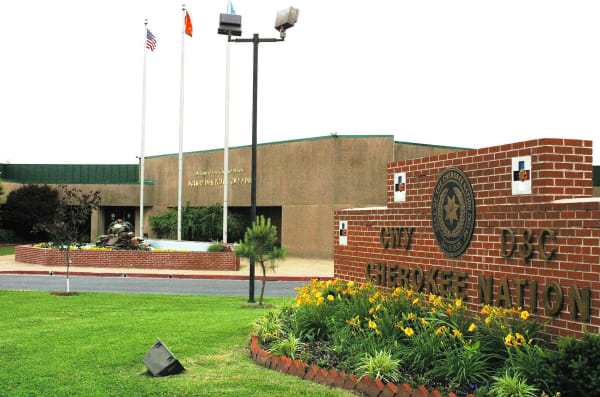The Cherokee Nation tribal complex in Tahlequah behind a brick sign that carries the Nation name in Cherokee syllabary and English beside its seal.
