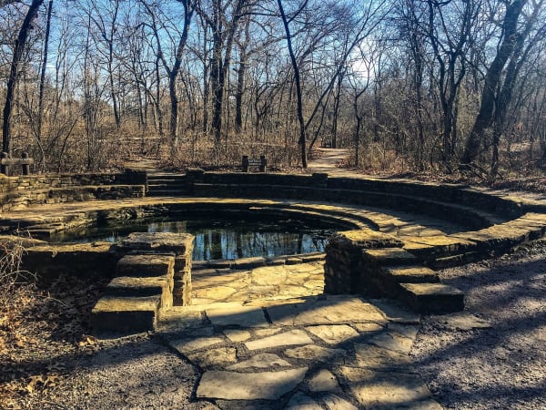 A stone-walled spring pool among bare winter trees in Chickasaw National Recreation Area at Sulphur.