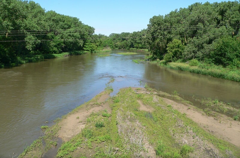 The Republican River runs between wooded banks and a grassy sandbar, looking upstream from the bridge at Red Cloud in Webster County.
