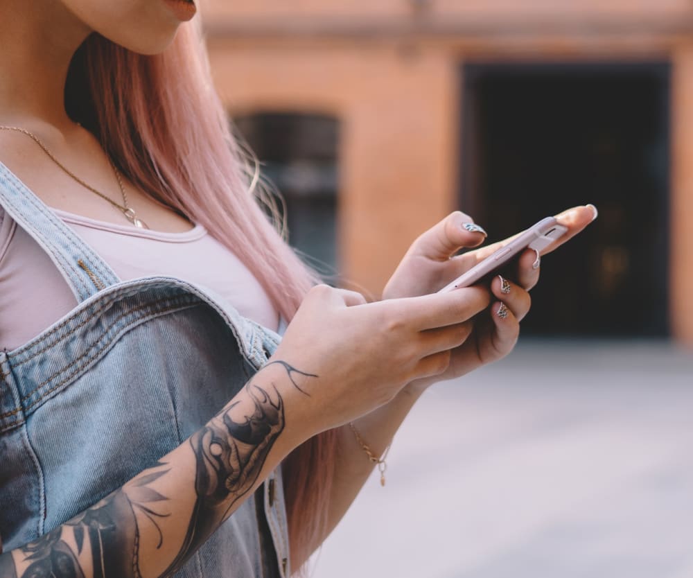 Kvinna med rosa hår och tatueringar använder mobil utomhus.