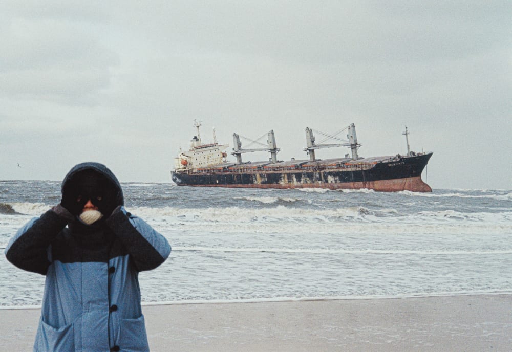 A person standing by the sea with a cargo ship behind