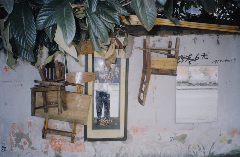 Wooden chairs hanging on a weathered wall beneath leaves