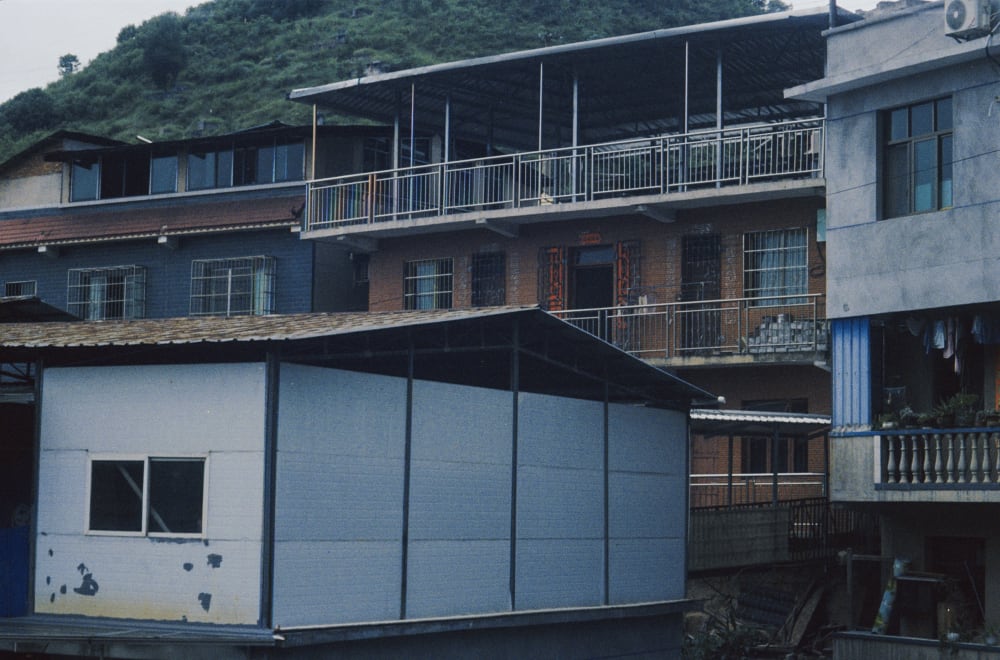 Apartment balconies and outbuildings beneath a wooded hill