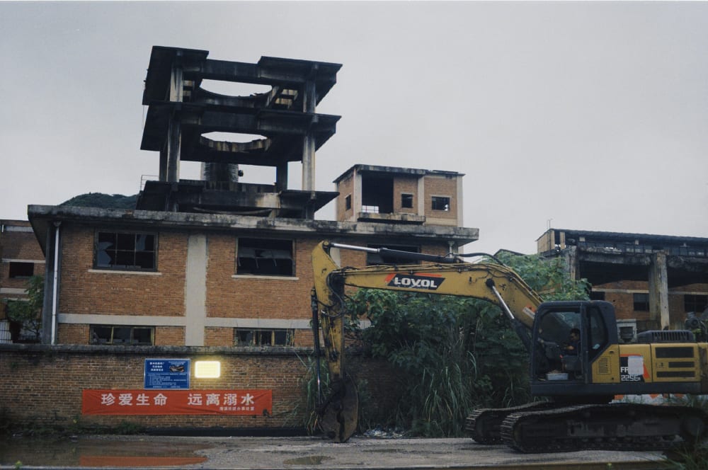 An excavator beside an abandoned industrial building