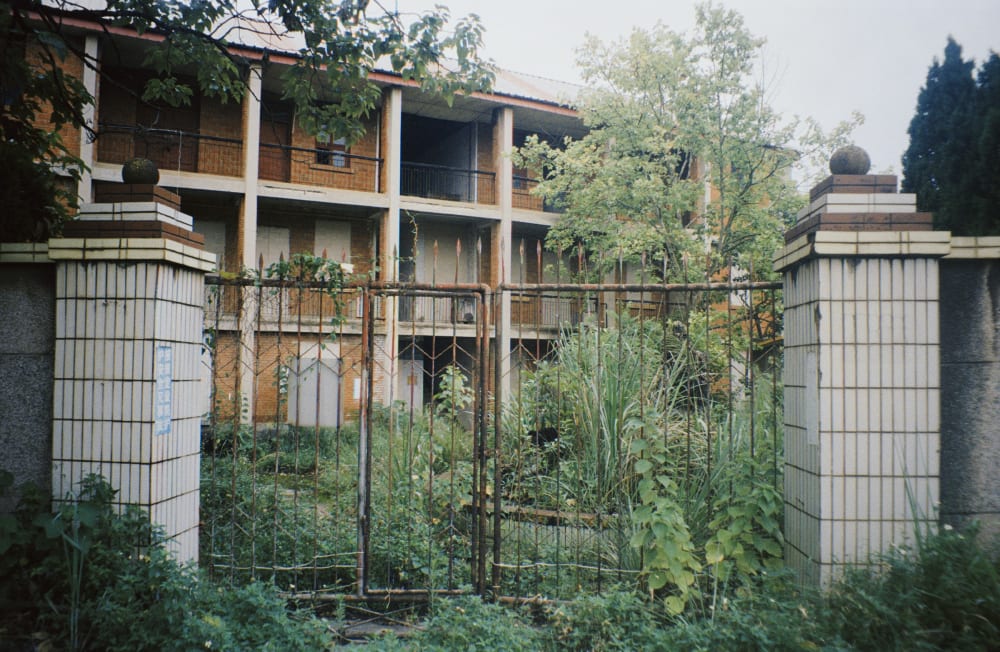 An overgrown gate in front of an empty brick building