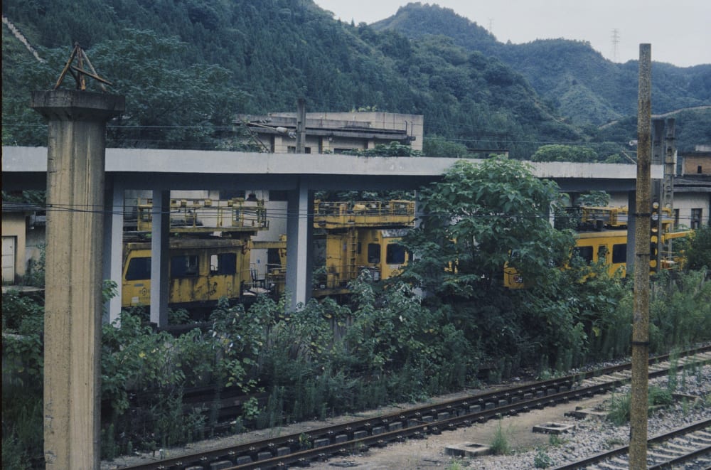 Yellow railway vehicles among trees and concrete columns