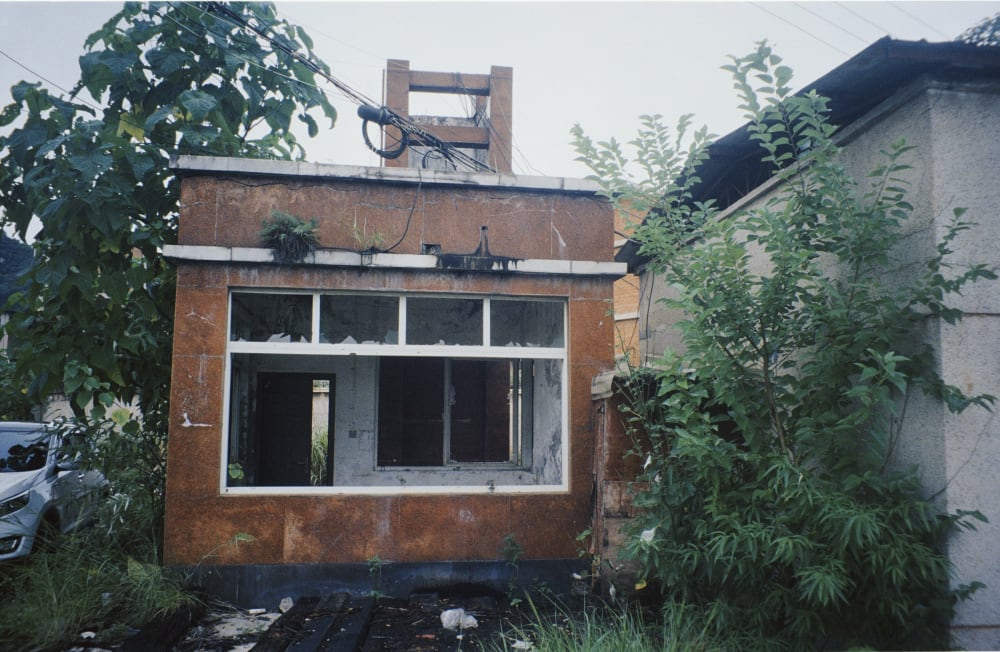 A vacant booth with broken windows surrounded by plants