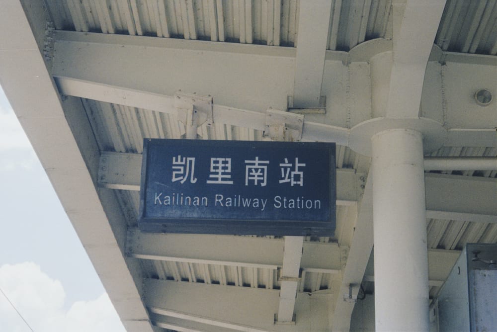A blue railway station sign beneath a platform roof