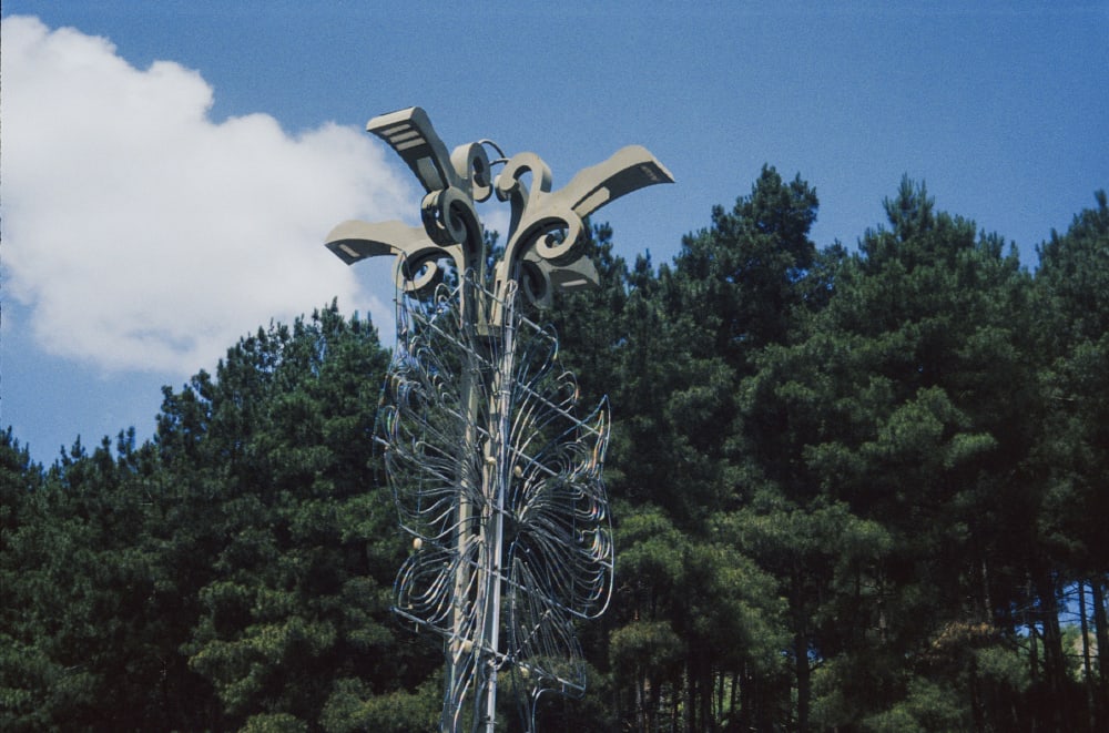 A metal sculpture against pine trees and a blue sky