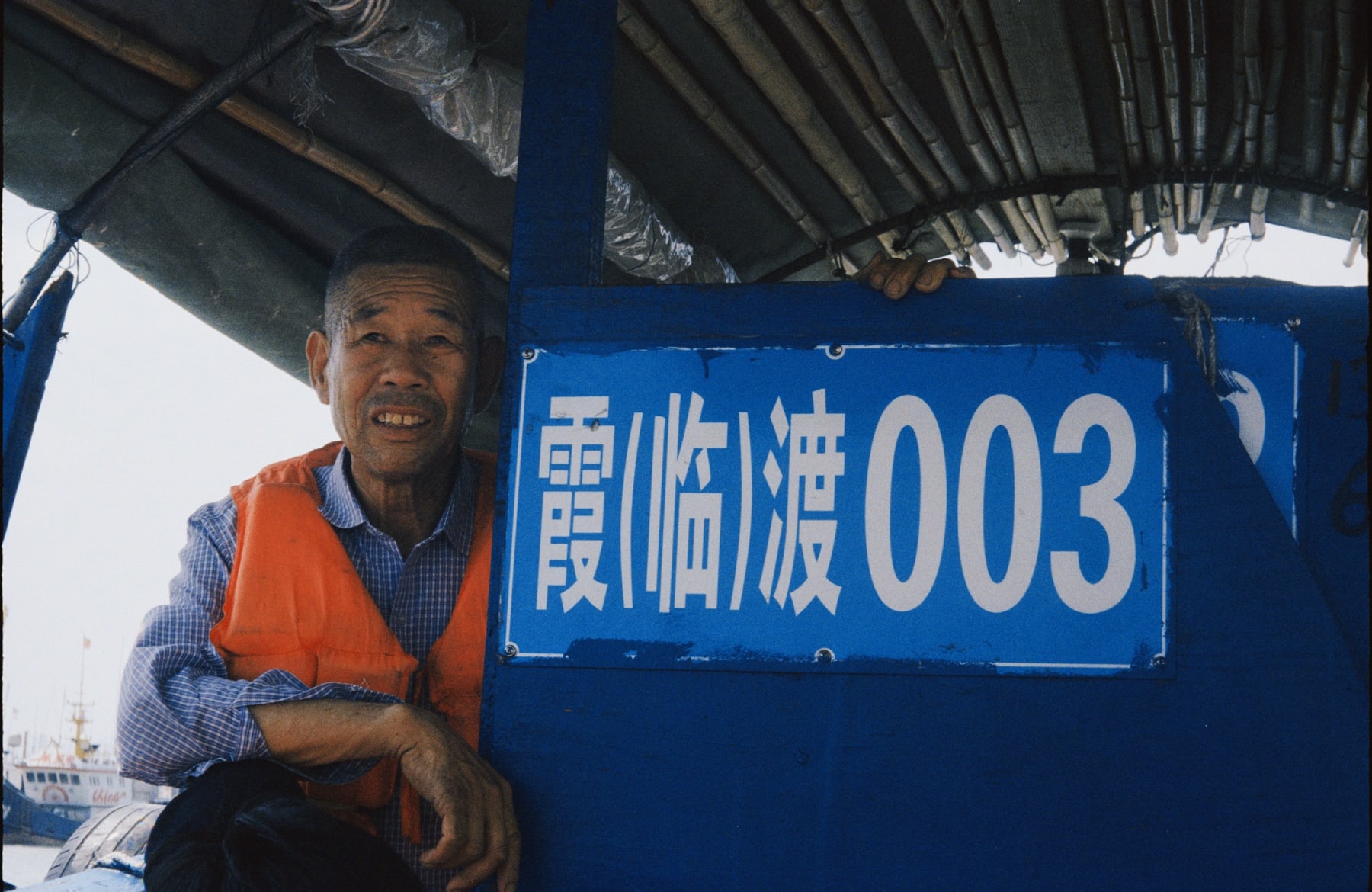 A smiling person beside a blue boat sign