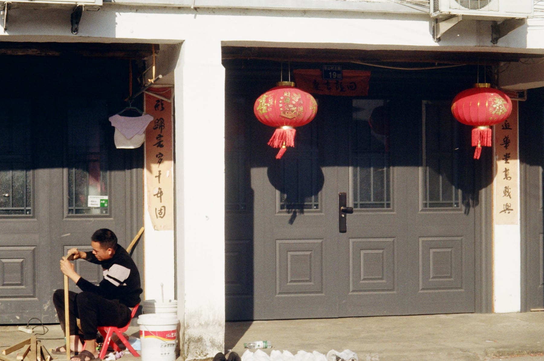 A man seated beside doors and red lanterns