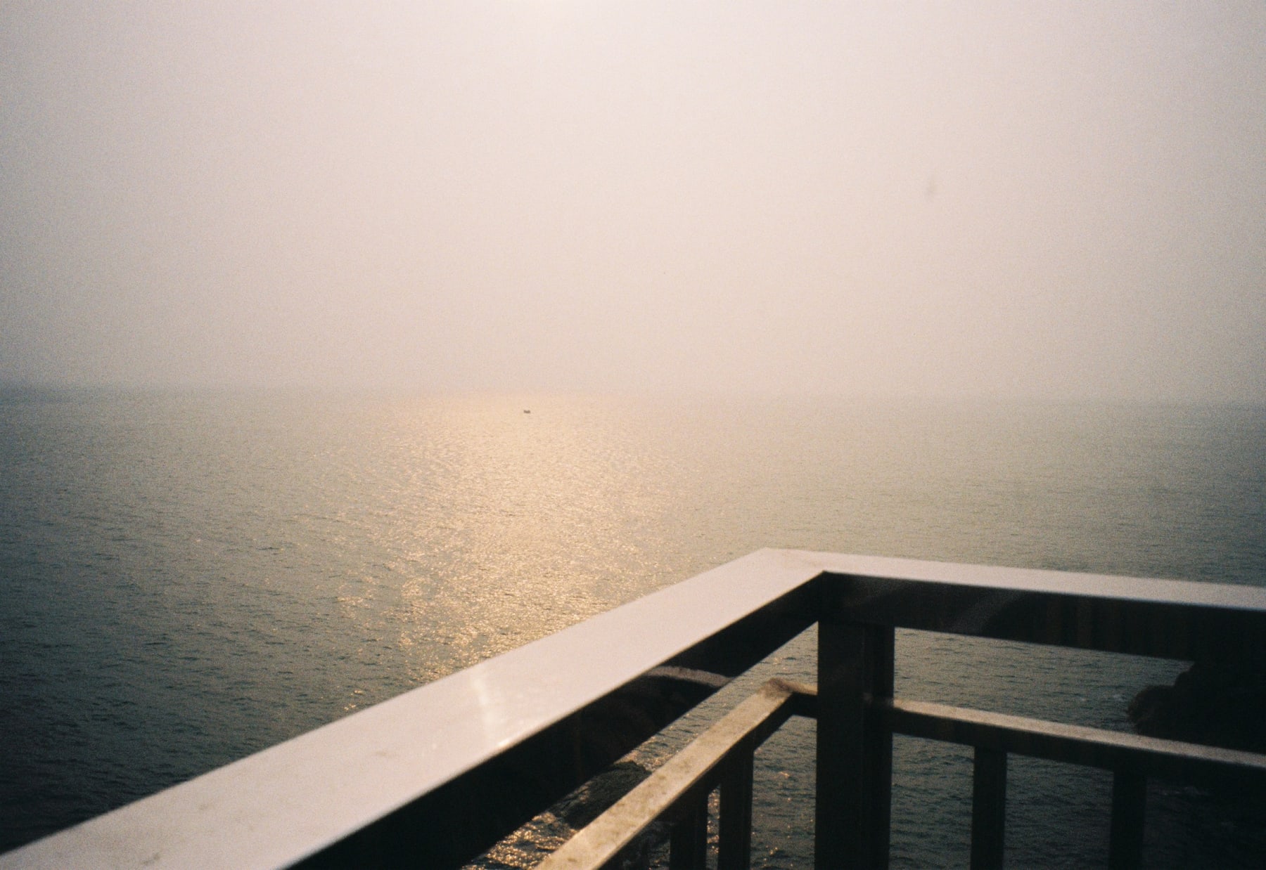 Sunlight over a misty sea beyond a railing