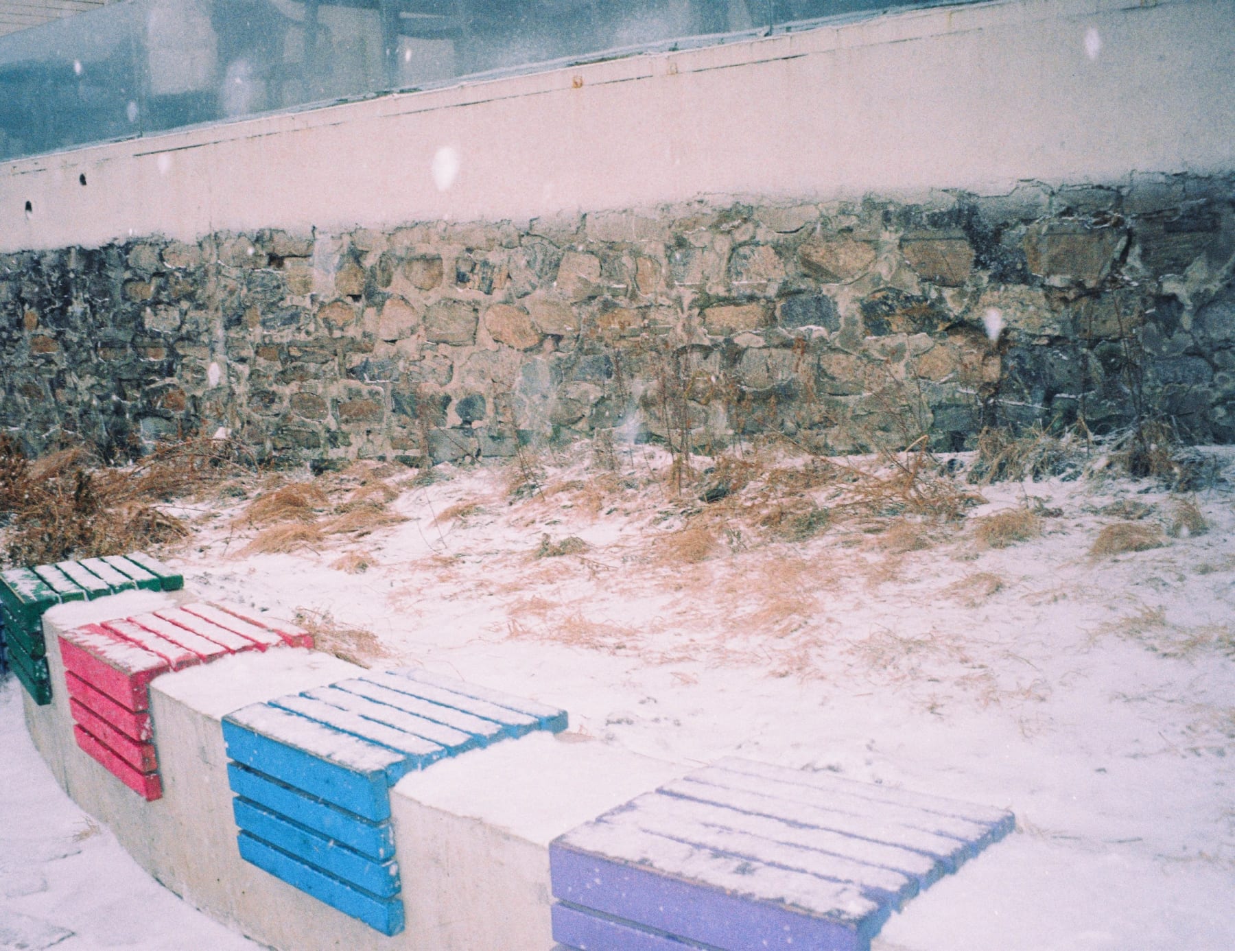 Colored benches beside a snowy stone wall