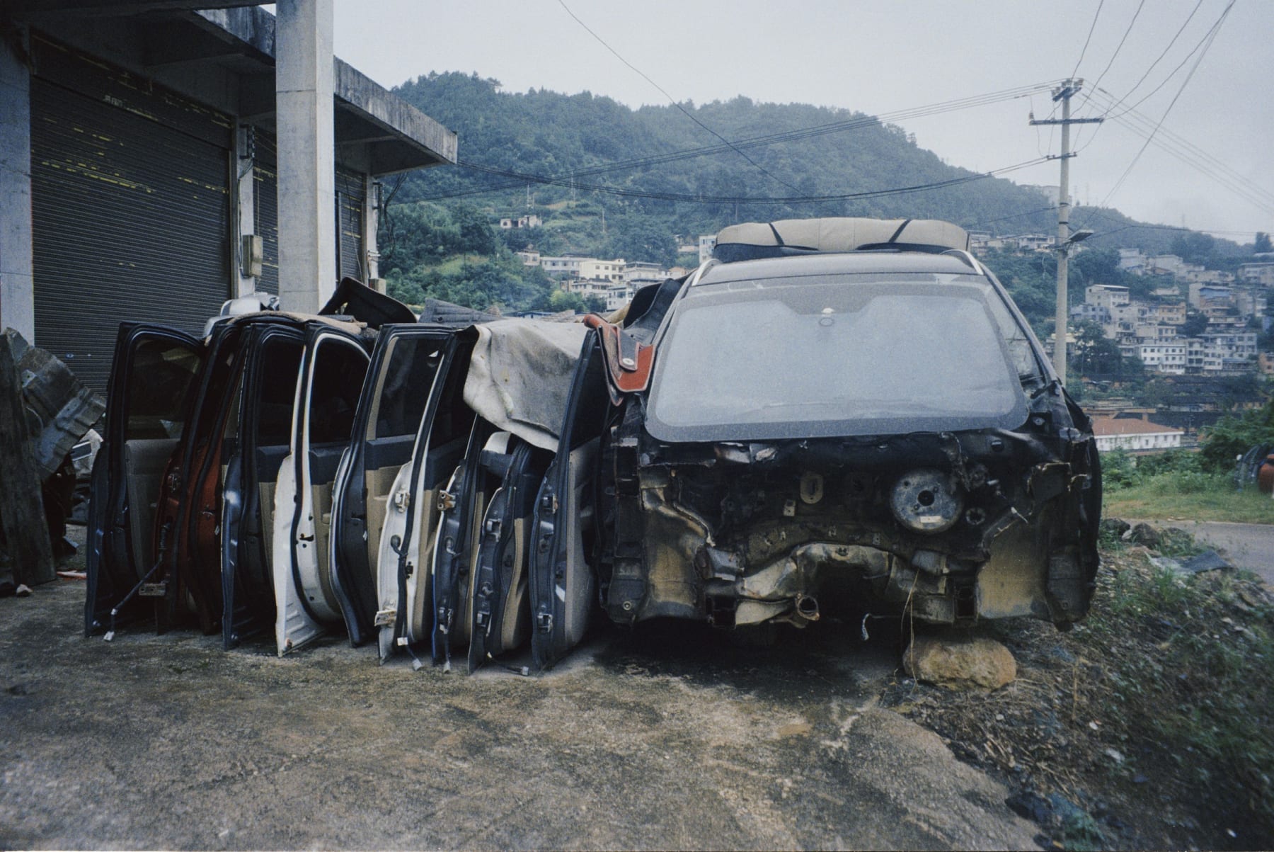A stripped car and detached doors beside a hillside neighborhood