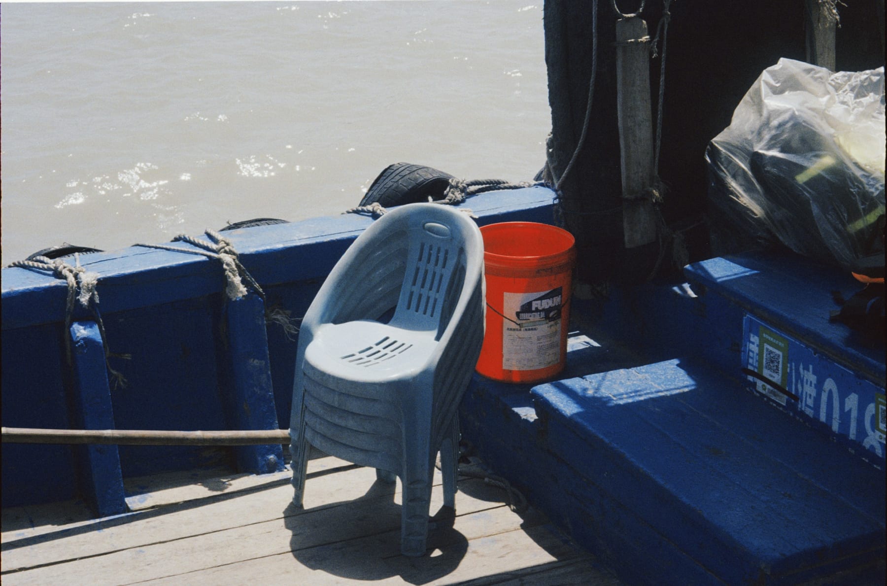 Stacked plastic chairs and an orange bucket aboard a blue boat