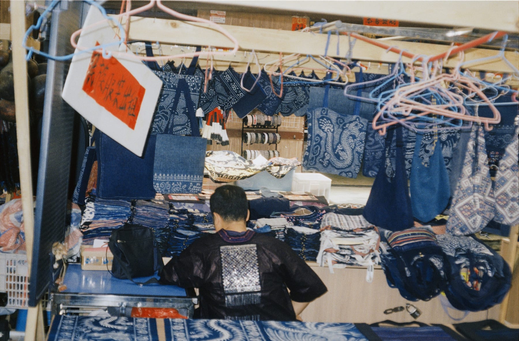 A person seated at a stall selling blue patterned textiles