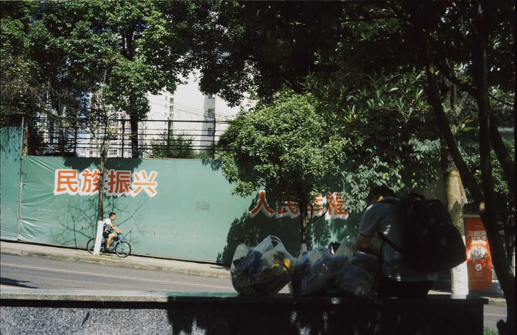 A cyclist passing a green wall while a person carries bags