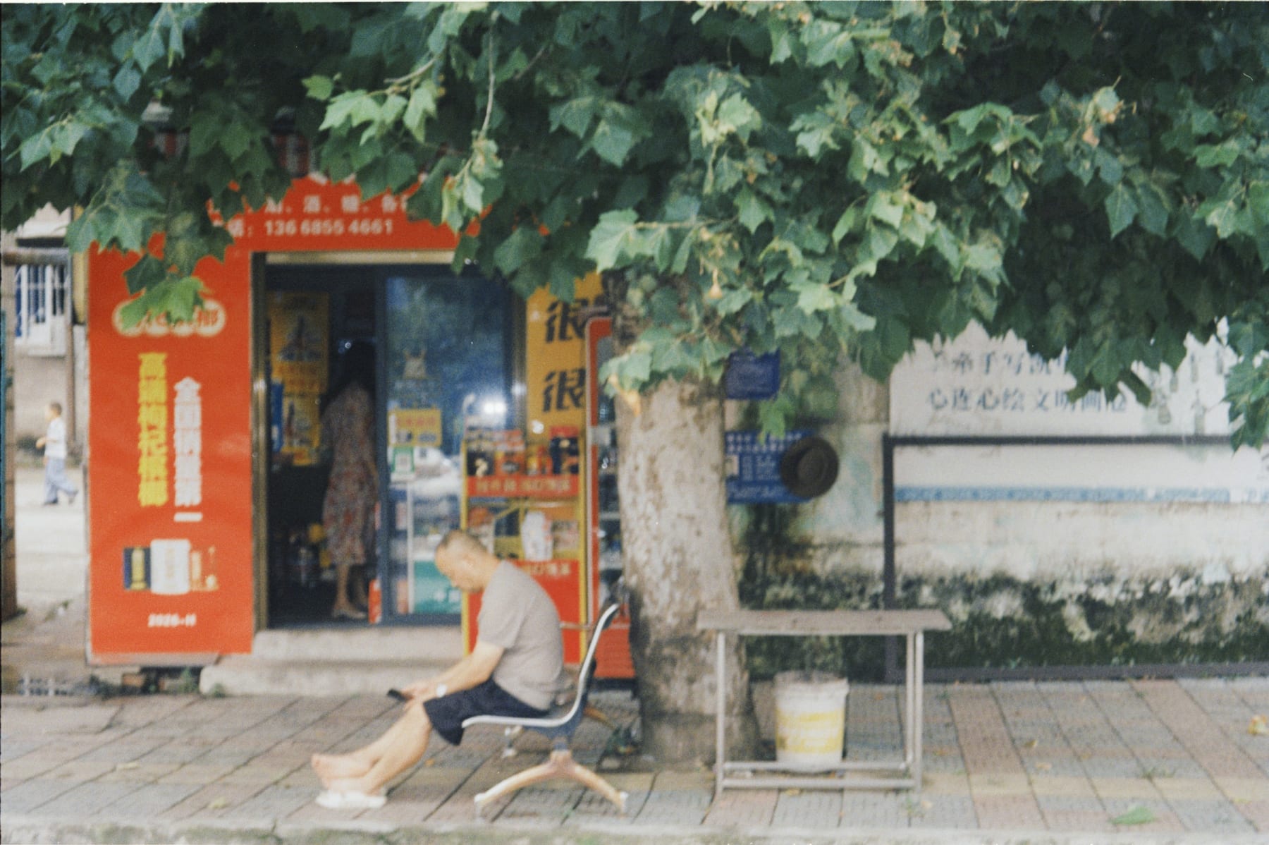 A person seated outside a shop beneath a tree
