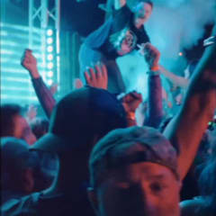 Dancers with hands raised in close teal and cyan lighting at a bass show