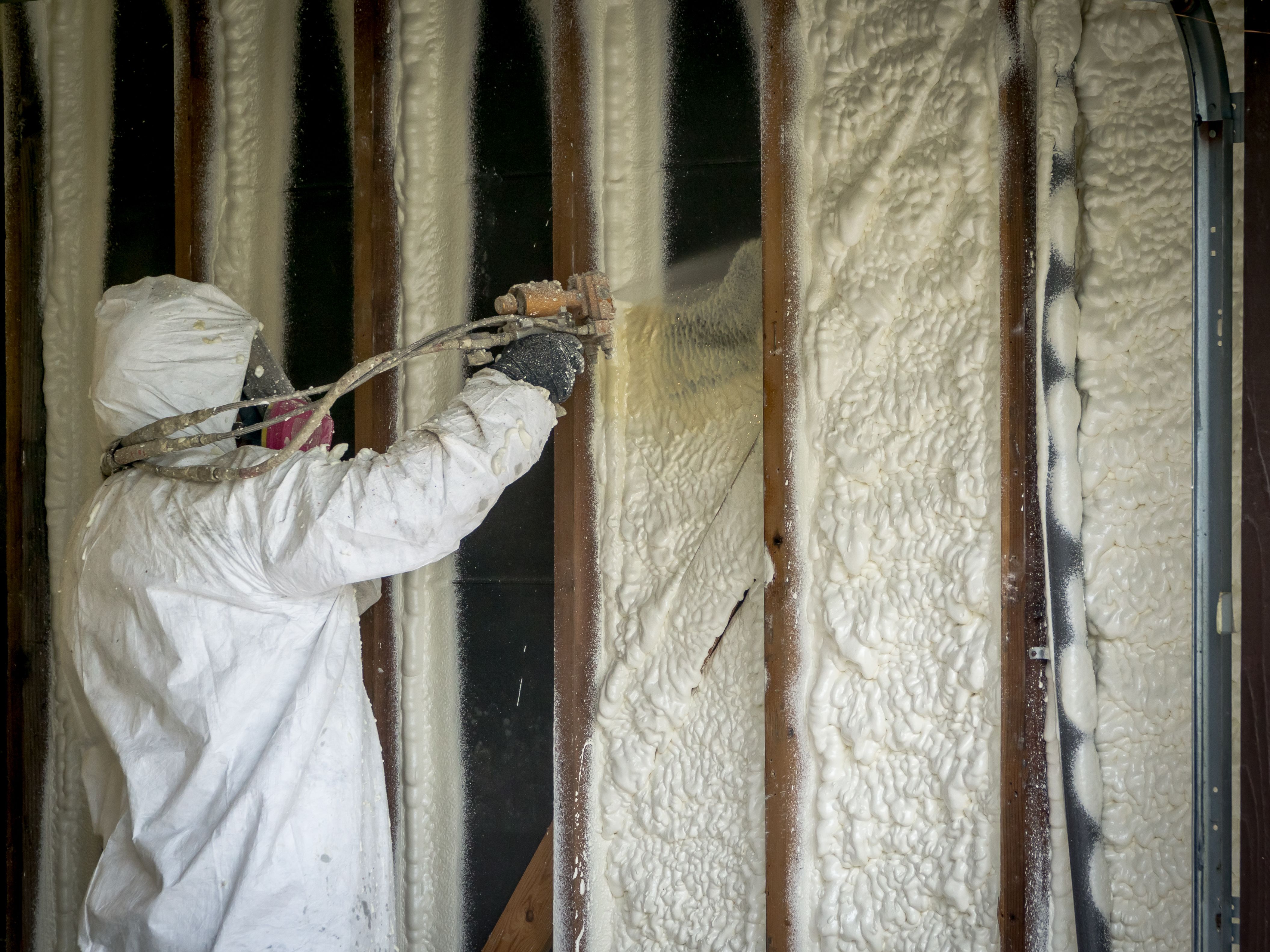 Man in gas mask and full body suit spraying spray foam insulation