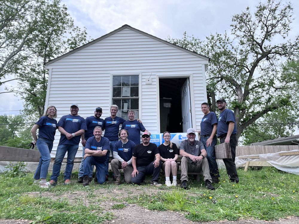 Knauf employees and Steadfast Veterans volunteers sitting in front of a newly built home for veterans in need.