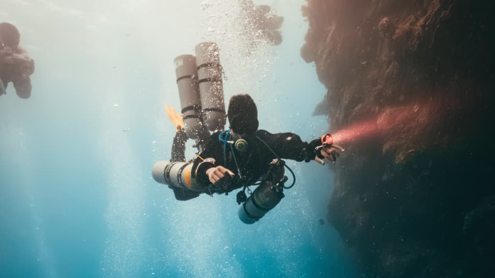 Koh Tao Divers technical diving student explores a narrow underwater cave passage with a flashlight