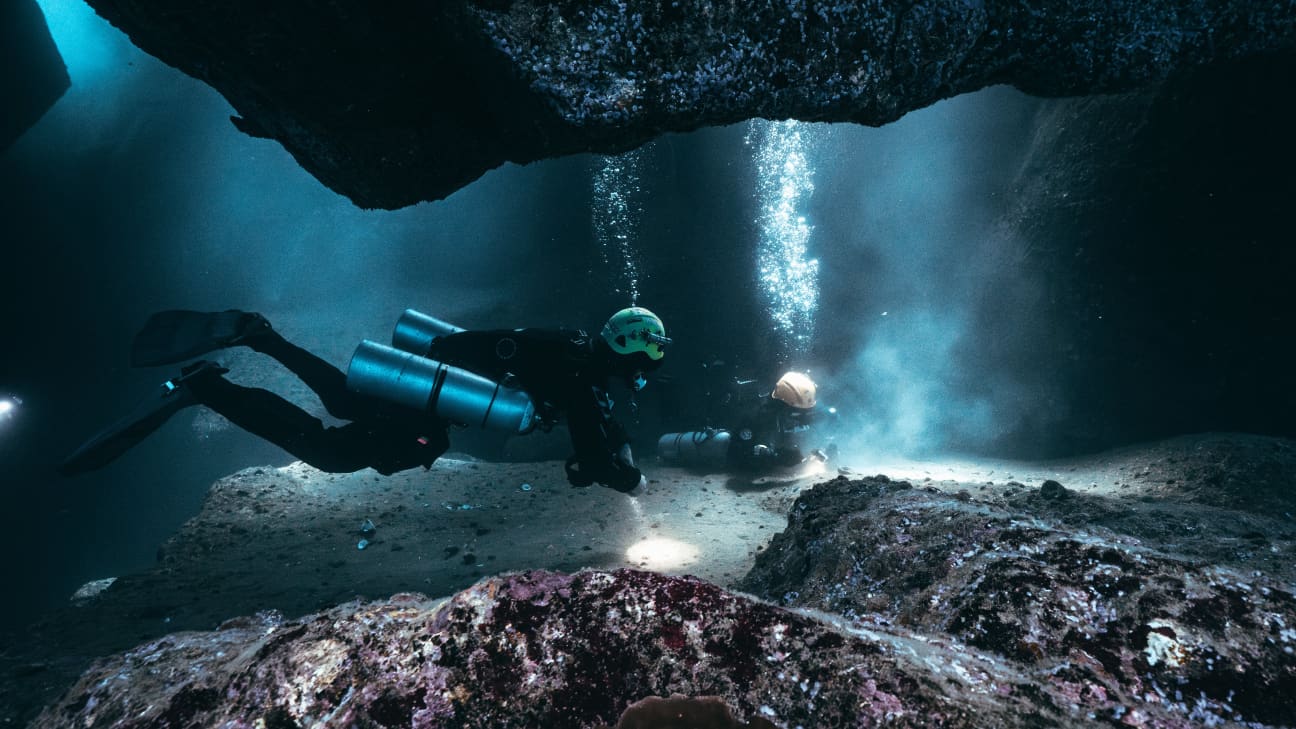 Koh Tao Divers exploring an underwater cavern passage with torchlights in low light conditions