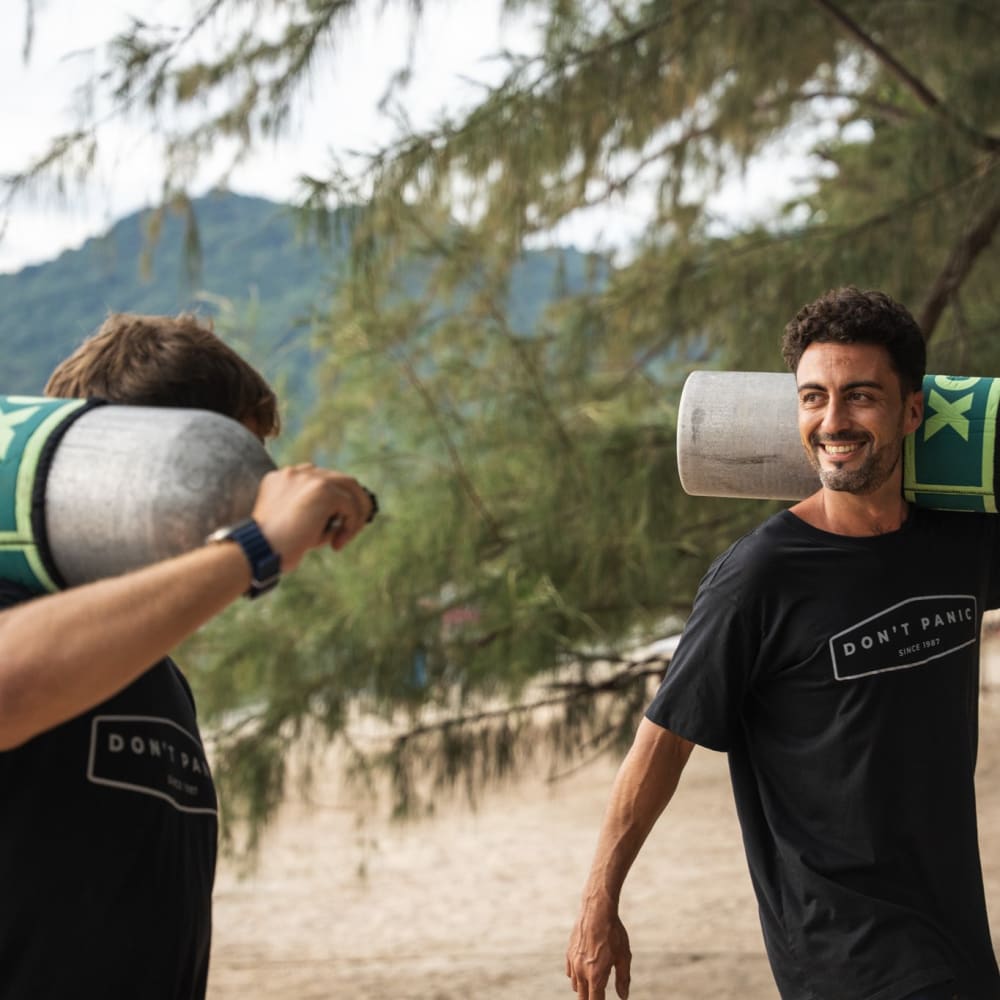 Koh Tao Divers instructor and student smiling while carrying scuba tanks on shoulder at the beach