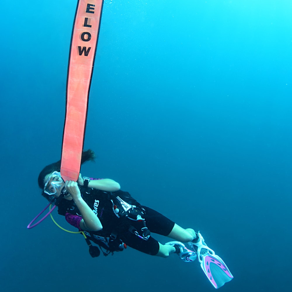Koh Tao Divers female diver signaling with fully inflated SMB marked "Diver Below"