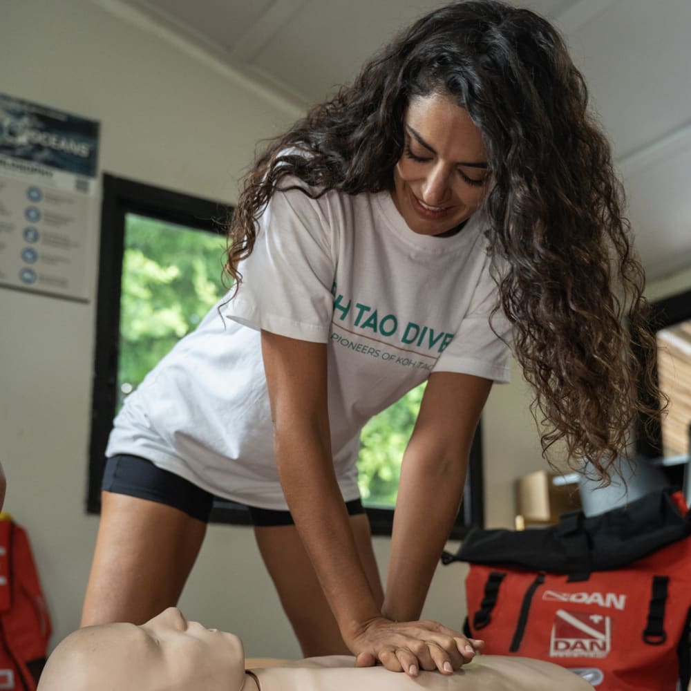 Koh Tao Divers first aid training with female instructor demonstrating CPR on a mannequin.