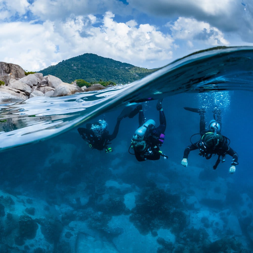 Koh Tao Divers group of scuba divers descending near rocky island shoreline