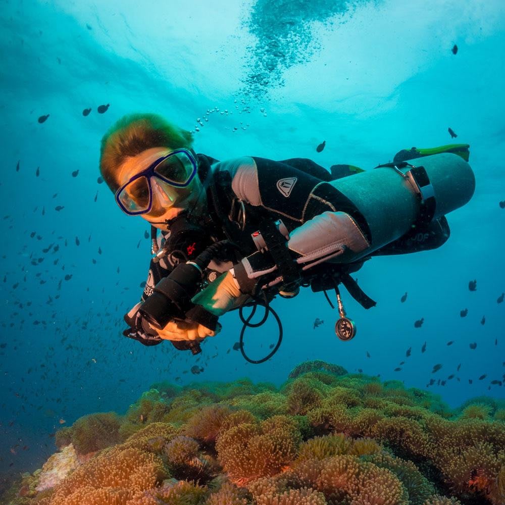 Koh Tao Divers technical diver underwater with twin tanks over colorful reef.