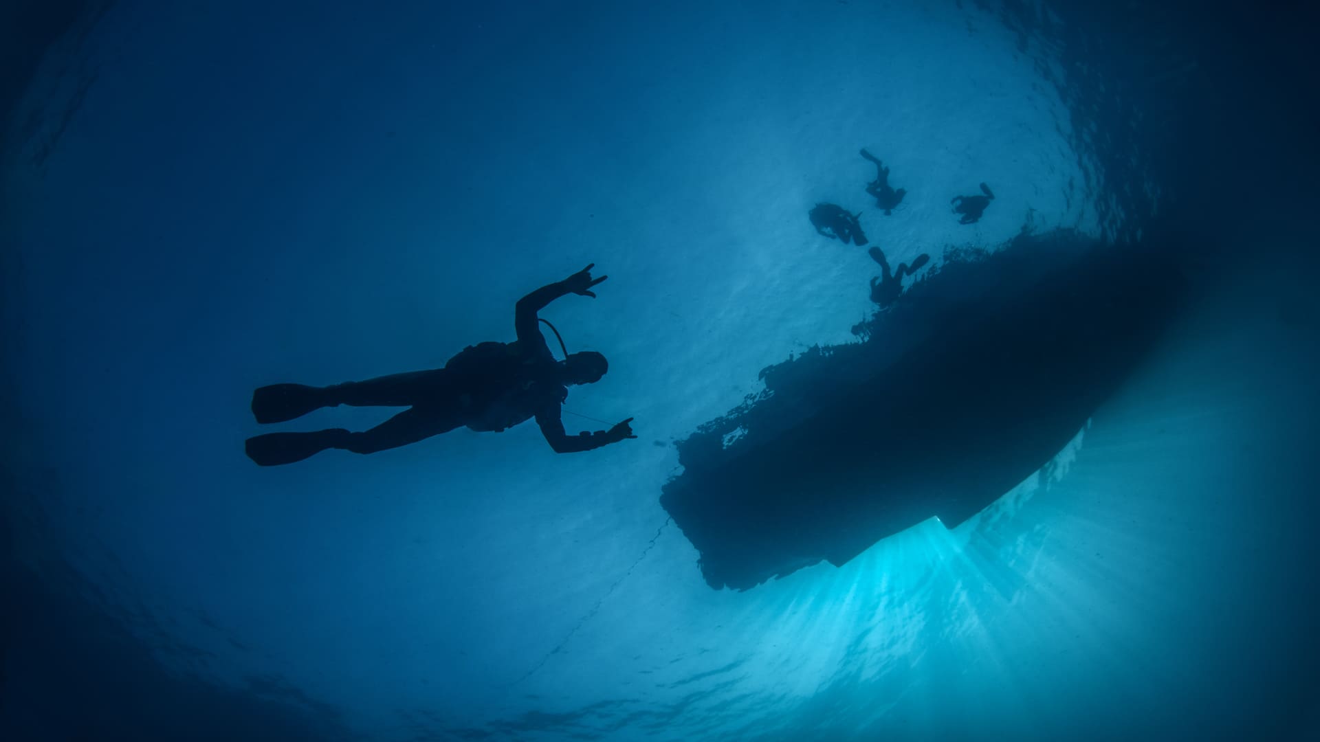 Koh Tao Divers scuba diver silhouetted against the sunlit surface with other divers near the boat above.
