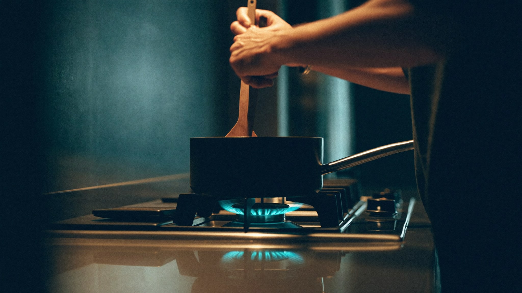 Mani che cucinano su un piano cottura a gas la sera